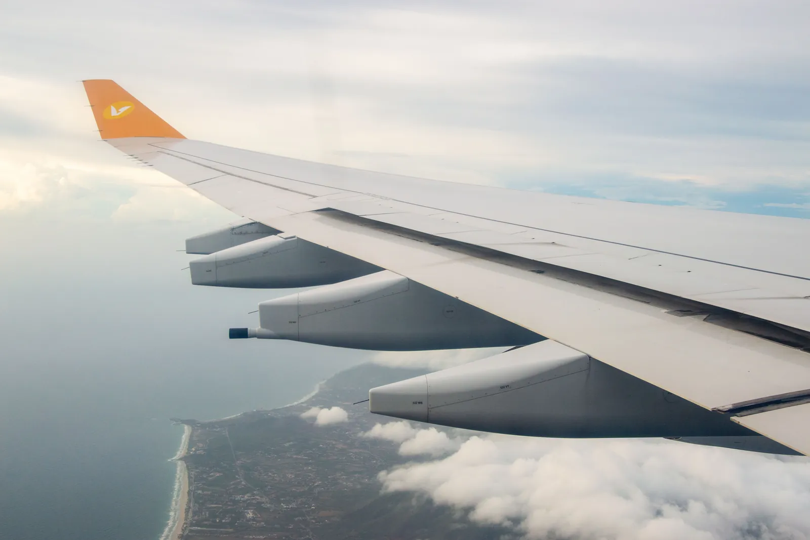 An aircraft wing above the coast and the clouds